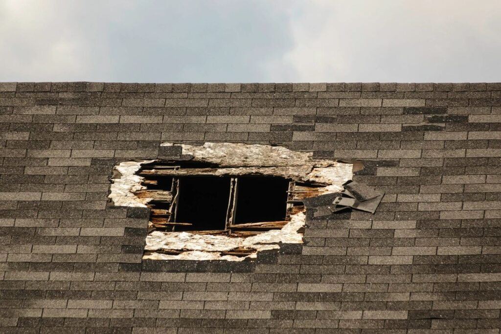 Damaged roof with large hole and missing shingles.